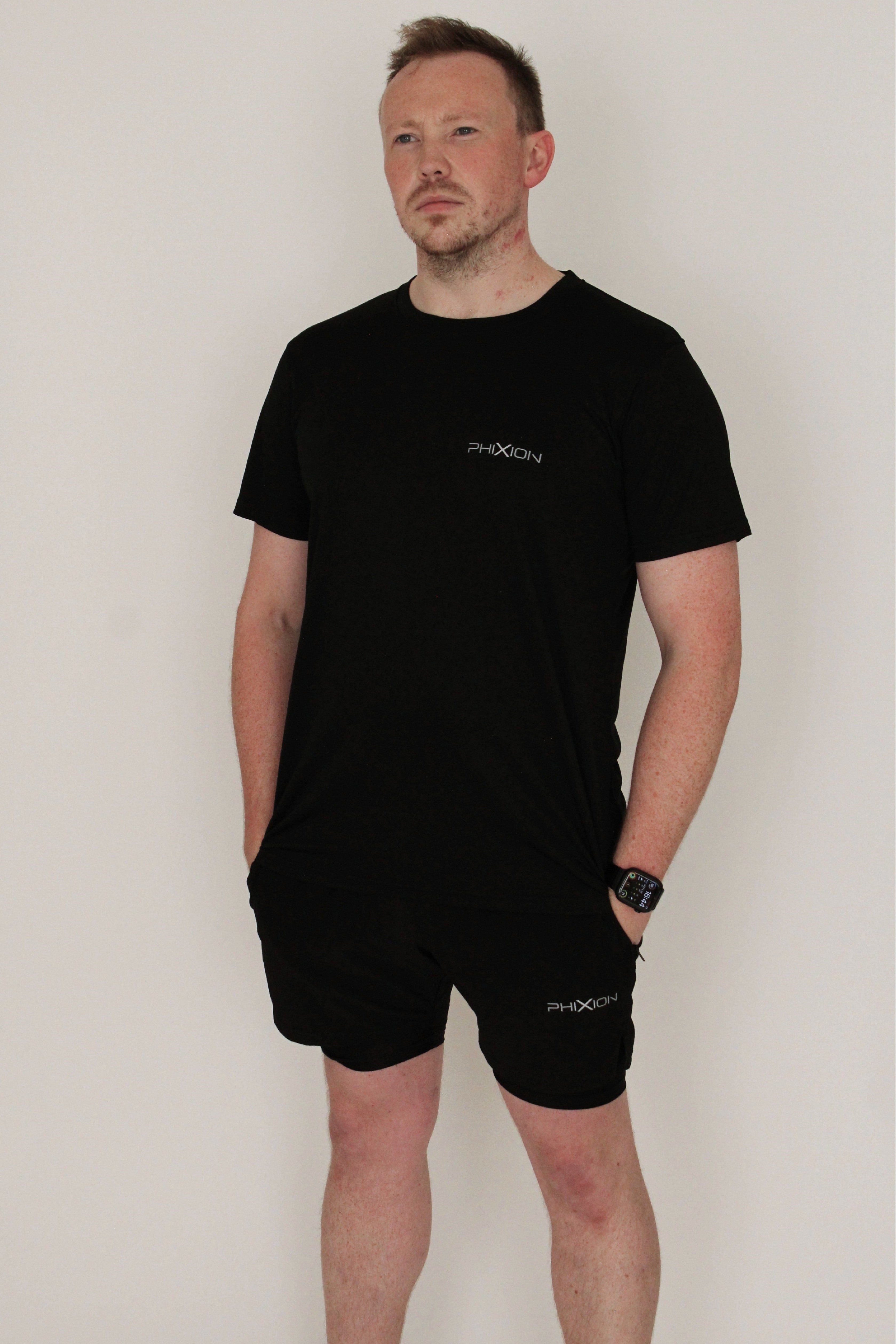 Model wearing Phixion Twin Skin Shorts in black against a white background. Athletic fit showcases the performance design.